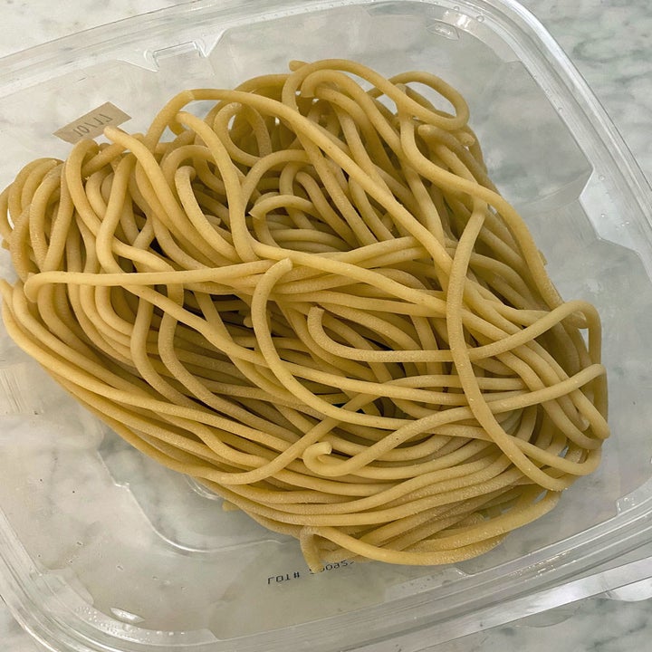 Fresh uncooked bucatini pasta in a plastic container.