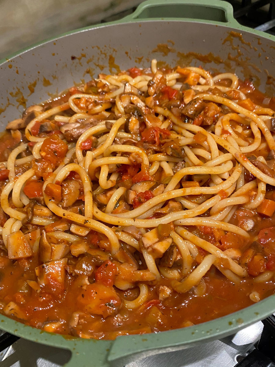 The bucatini mixed in with the Bolognese sauce in a pan/