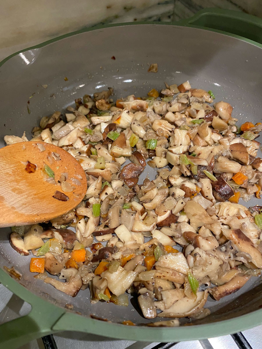 Mushrooms browning in a skillet with cooked carrots, celery, and onion.