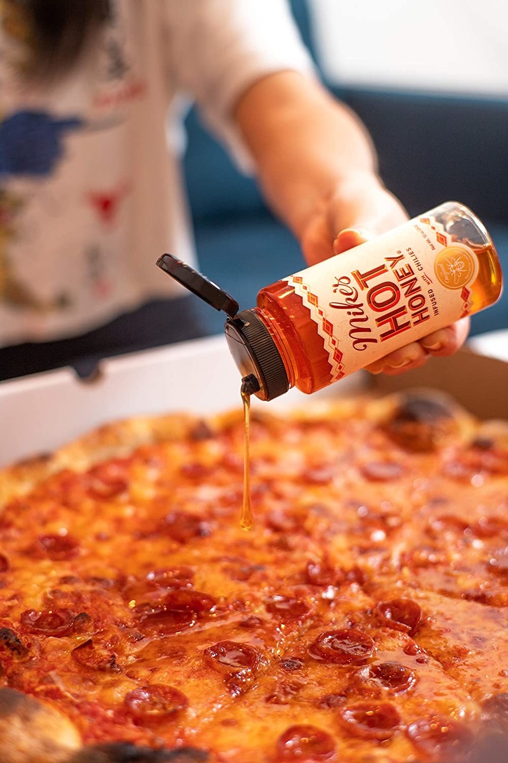 A hand drizzles the honey on a pepperoni pizza