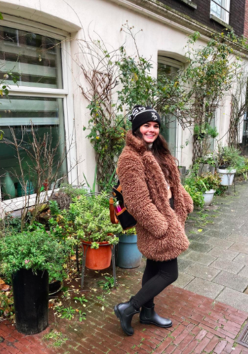 Reviewer wears black Chelsea rain boots with black leggings, a brown teddy coat, and a black beanie while enjoying a rainy day in Europe