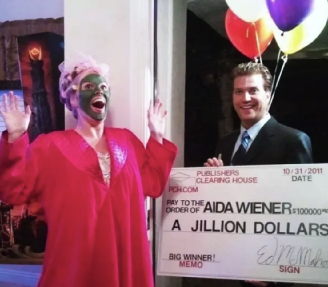 A woman dressed as a Publishers Clearing House winner (robe and face mask and all), and a spokesperson with a giant check