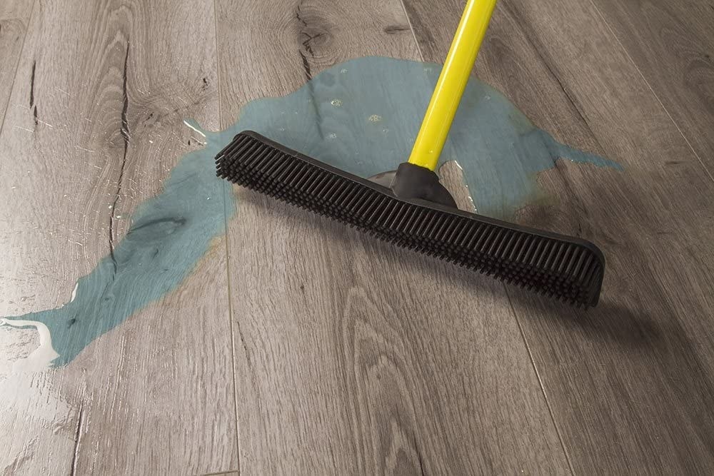 The broom with its edge cleaning up a spill on a hardwood floor 