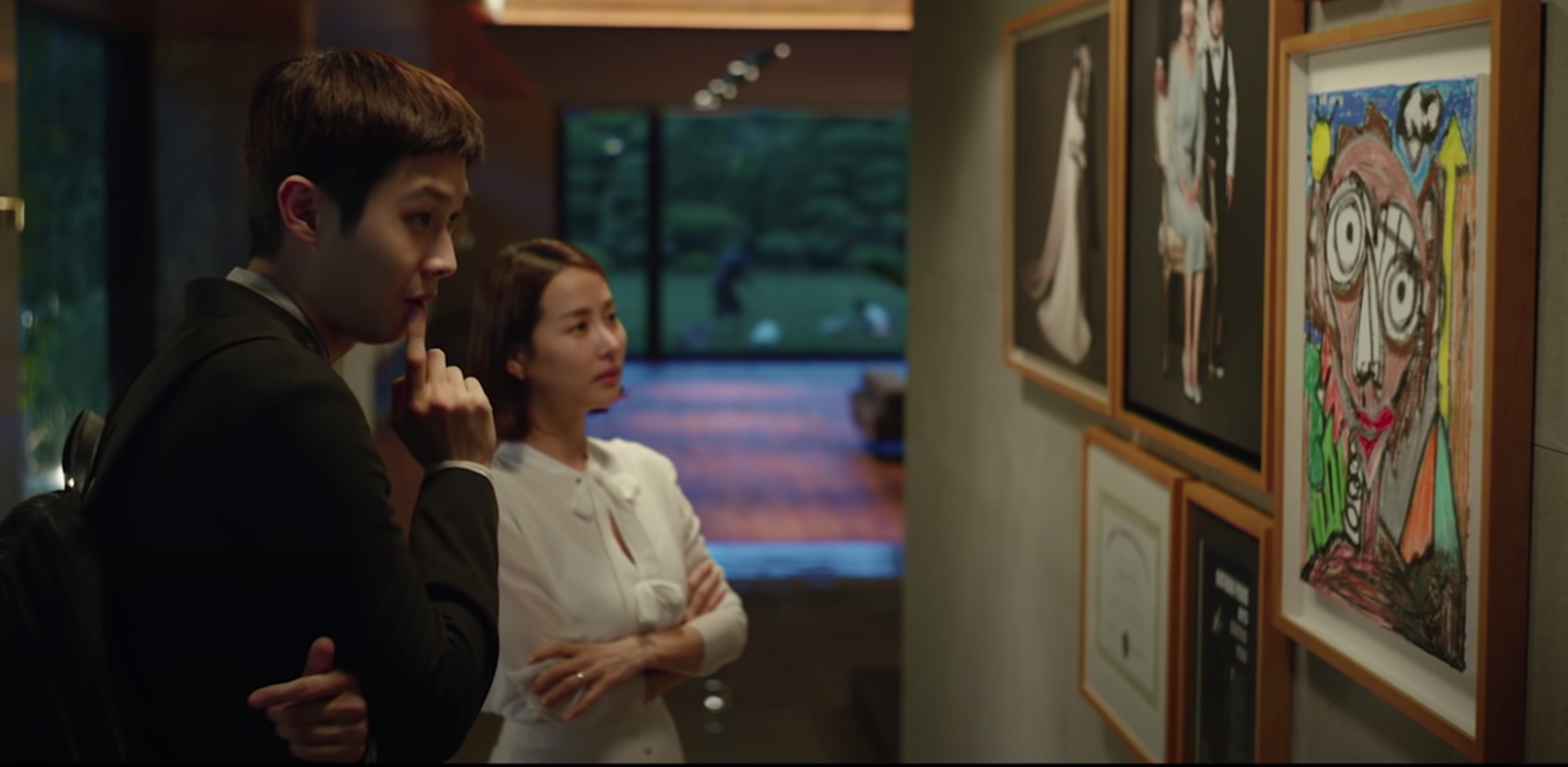 Kim Ki-woo and Choi Yeon-gyo examine art that was done by Yeon-gyo's son
