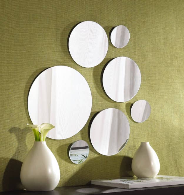 Big and small circle mirrors hang from a green wall above a wooden dresser