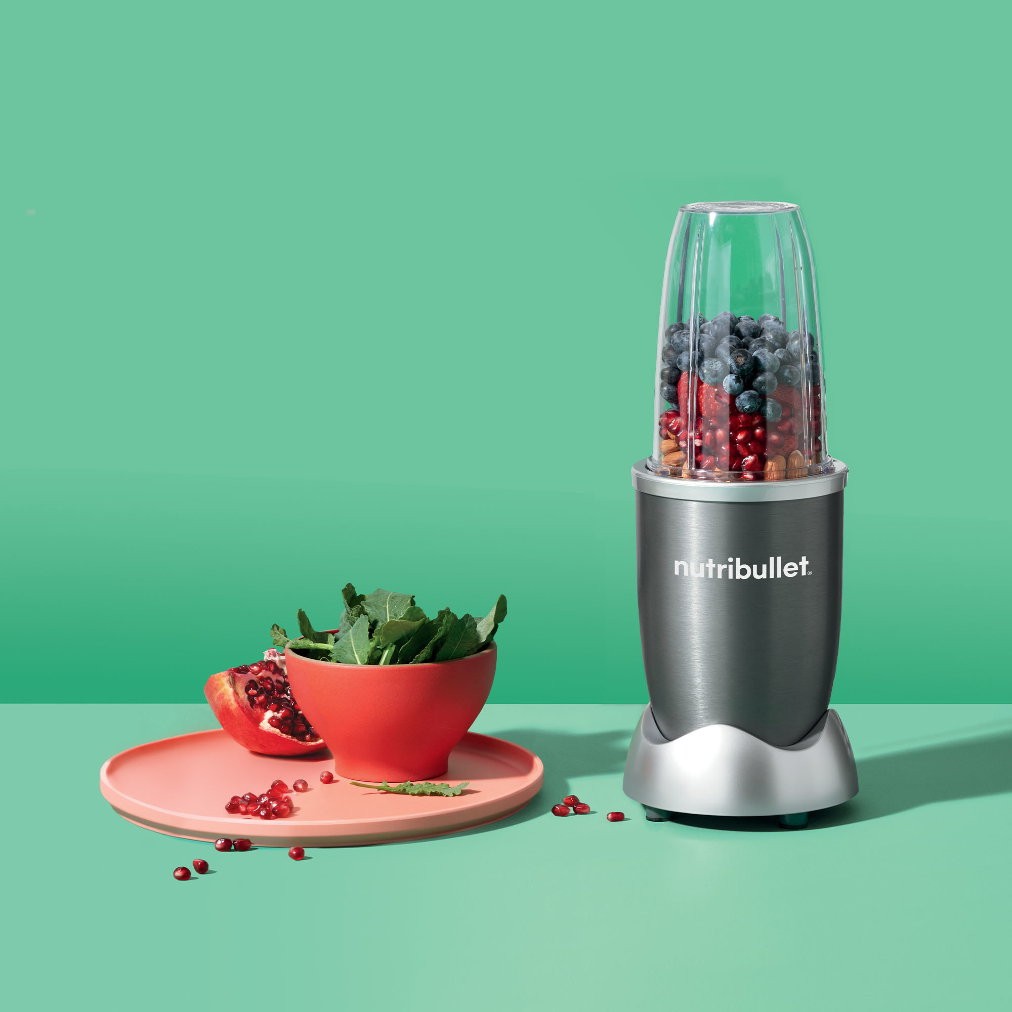 The blender filled with fruit next to a bowl of leafy greens