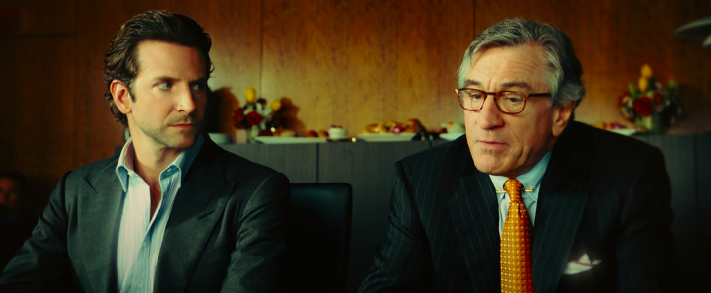 Bradley Cooper, in a dress shirt and jacket, next to Robert De Niro, who is wearing a business suit, but with a tie