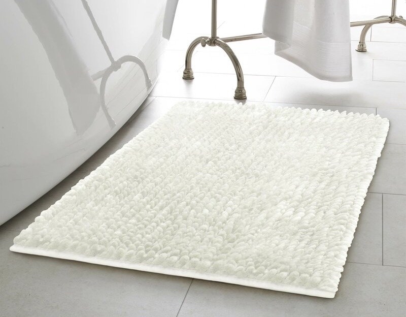 A white fluffy bath rug on gray tile in a bathroom 