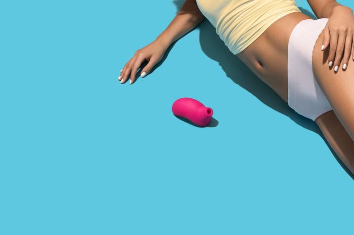 A model lies next to the LELO SONA clitoral massager while in their underwear