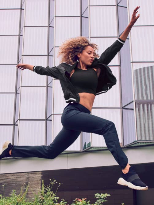 Model wears black Athleta Conscious Crop with black joggers, a hoodie, and sneakers