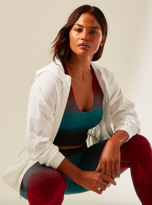 Model wears white running jacket with a green and red ombre crop top and running leggings