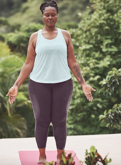 Model wears light blue vapor scoop tank with purple mesh leggings while standing on a yoga mat