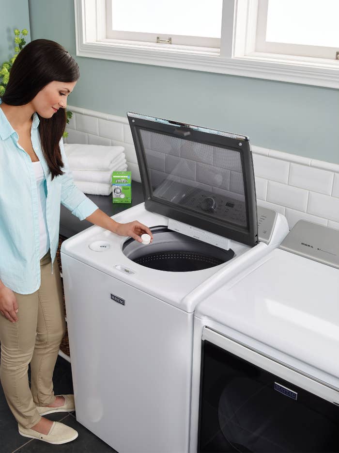 The cleaner, which is in tablet form, being dropped into a top-loading washer