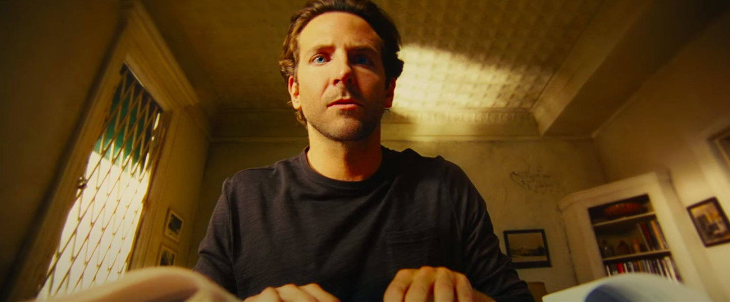 The camera is close to Bradley Cooper&#x27;s torso and looking up at him as he types in a long sleeve t-shirt