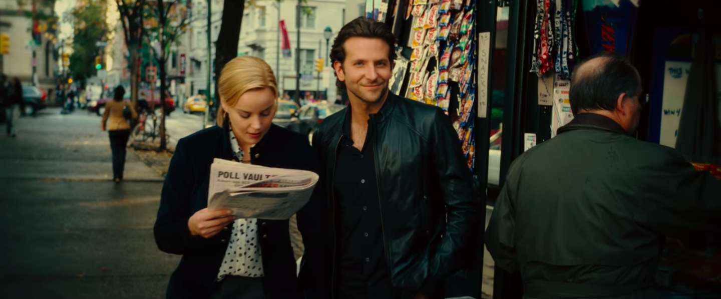 Bradley Cooper, in a button up and leather jacket, looking directly at the camera