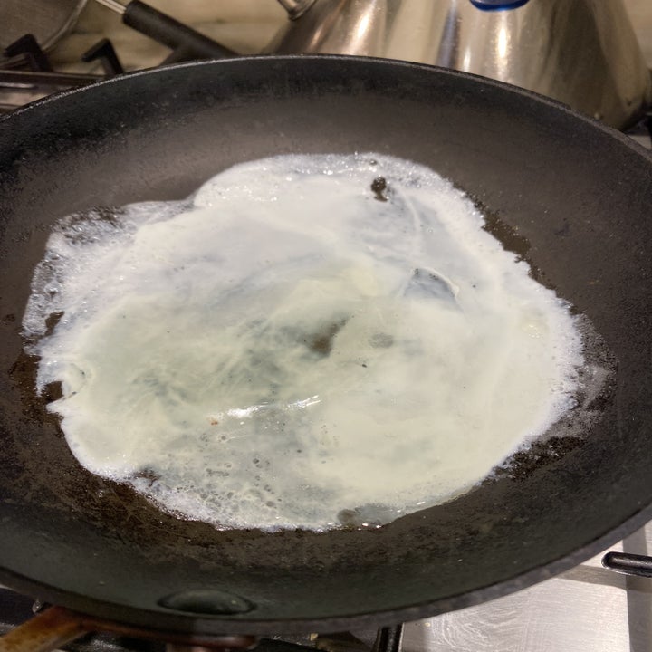 A thin ayer of egg white cooking on a skillet.