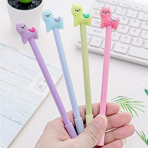A hand holding the lavender, blue, green, and pink pens with matching llama-shaped toppers and their caps on