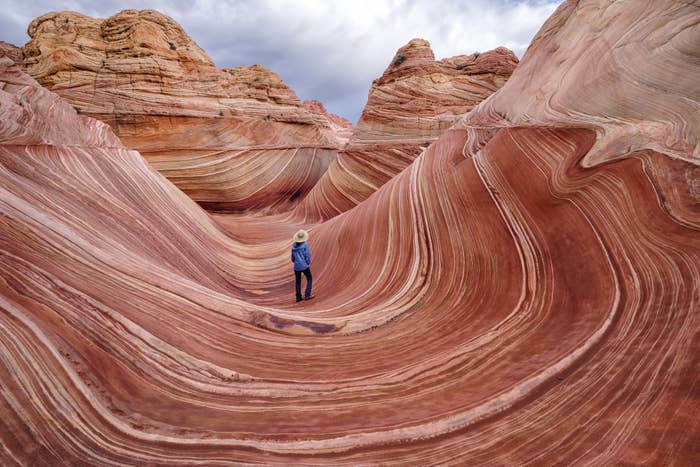 a person standing in an orange and brown rock formation that looks like a giant wave