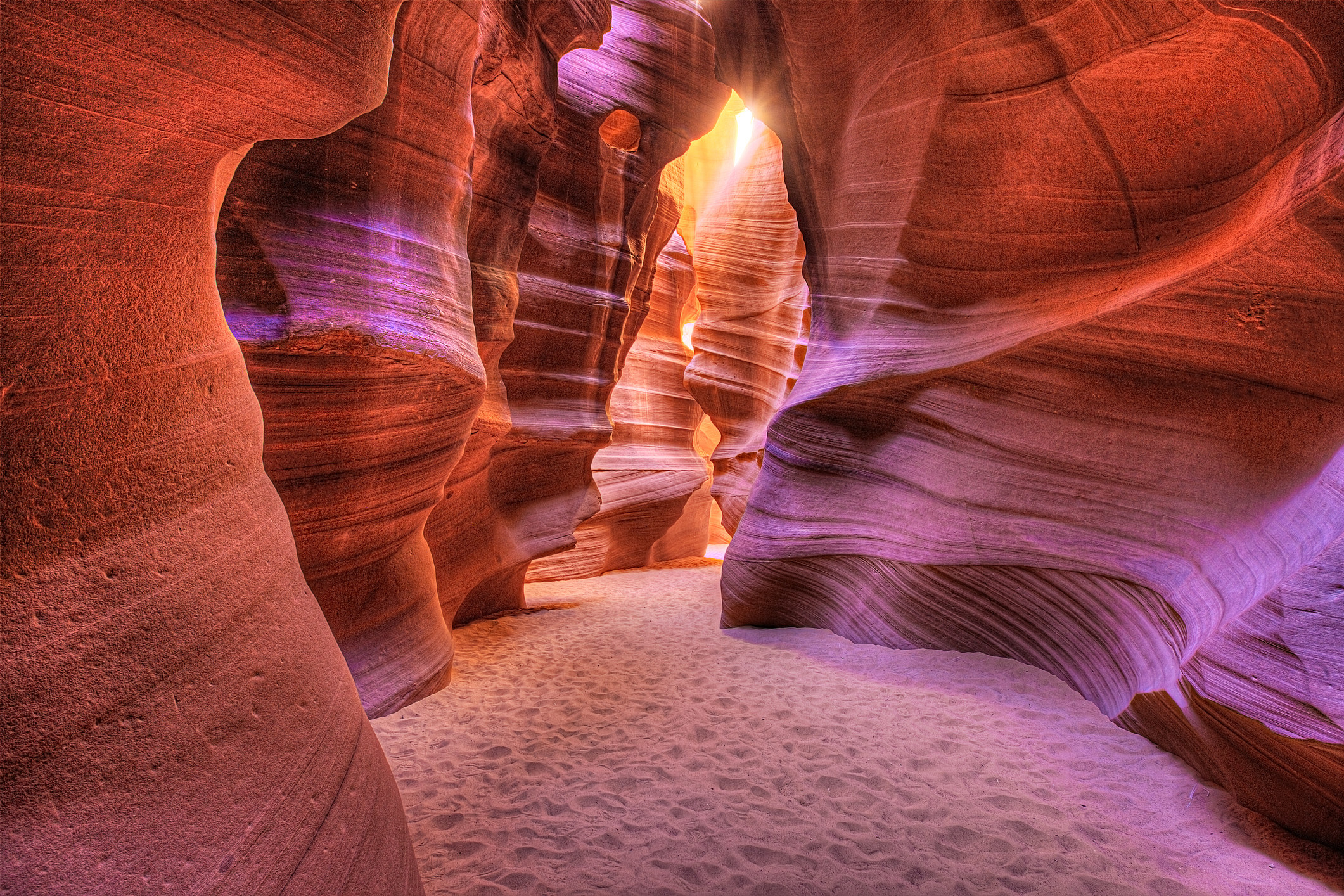 an underground canyon with vibrant colored walls and light shining through a crack in the roof