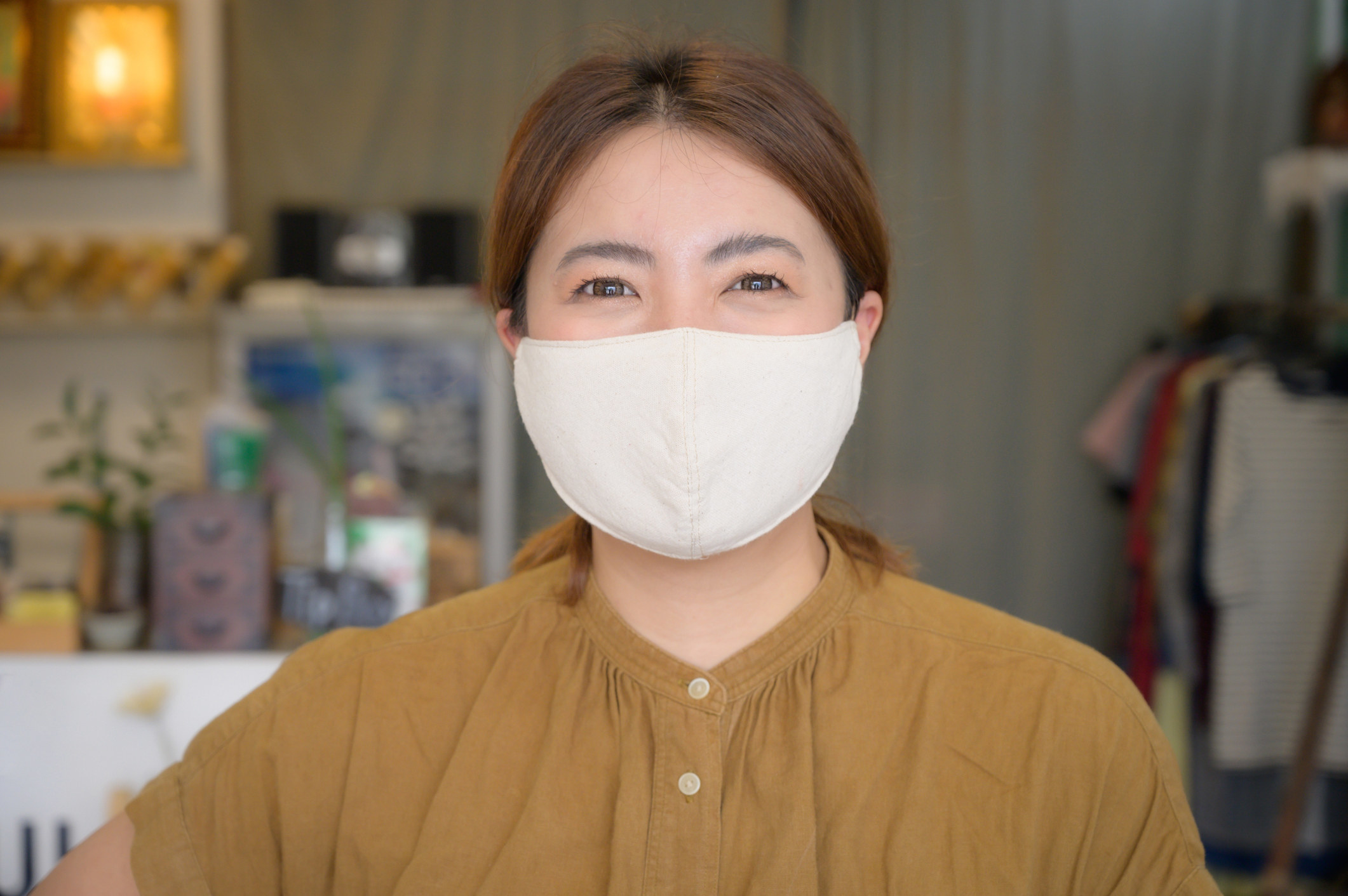 A person wearing a mock-neck shirt and smiling behind a simple neutral-toned mask