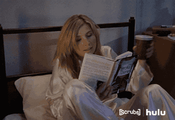 Woman snuggling down into bed with a book and hot drink