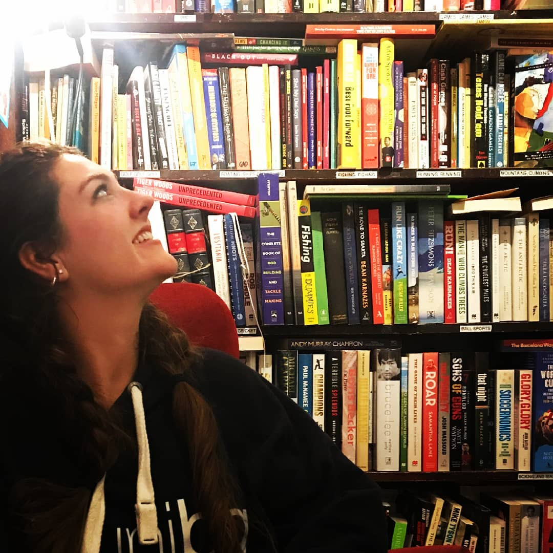 Woman with long dark hair looking up at a huge bookcase behind her