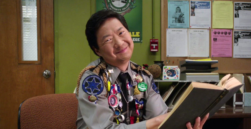 Chang smiling at the camera while holding an open book at his desk