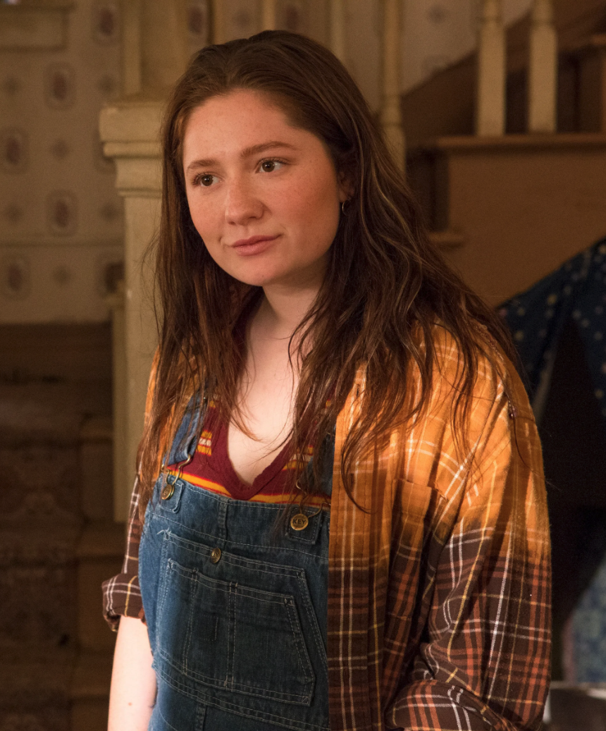 Debbie standing in her home; she is wearing overalls with a flannel on top