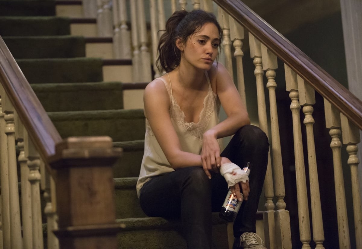 Fiona sitting on the stairs holding a bottle; her hand is wrapped in a bandage that has a bit of blood stained on it