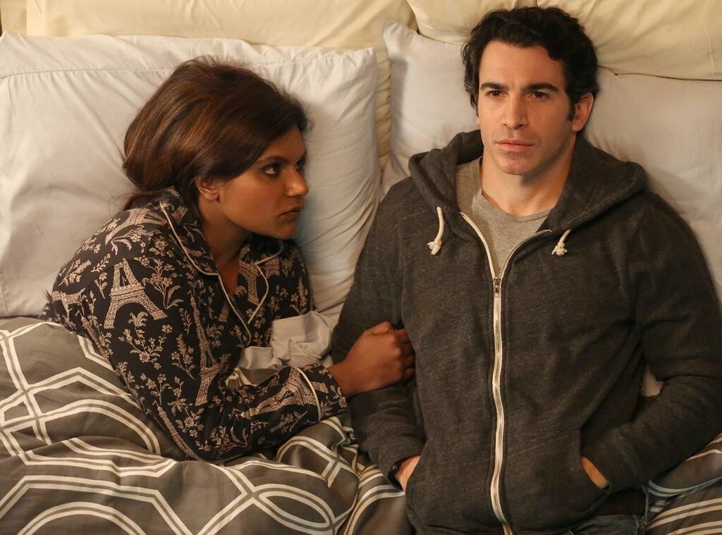 Mindy and Danny lying down in bed together; Mindy is holding Danny&#x27;s arm, while he looks straight into the distance