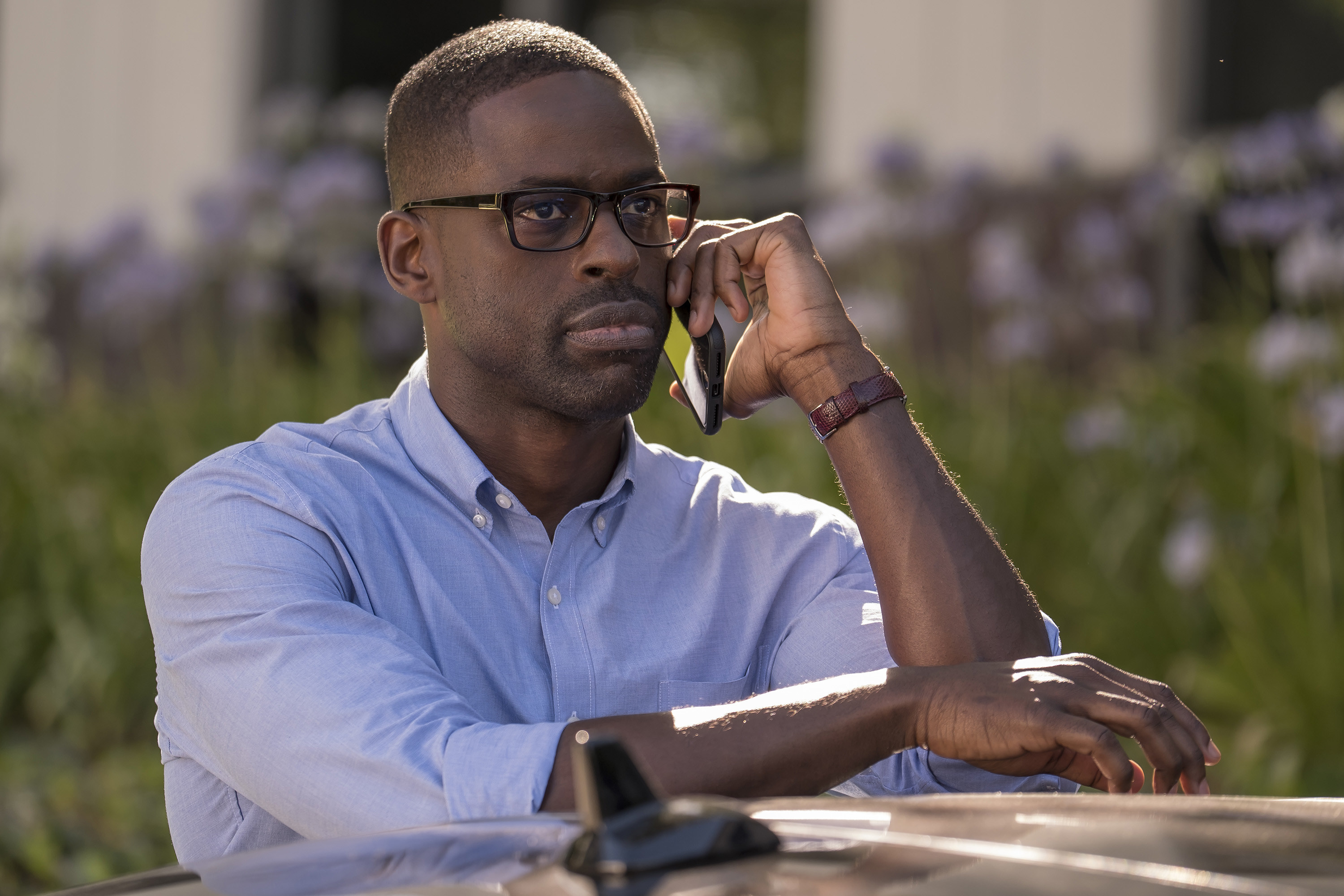 Randall sitting at an outdoor table; he is calling someone on his phone and looking into the distance