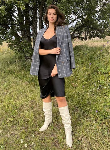 model wearing black slip dress with plaid blazer and white boots