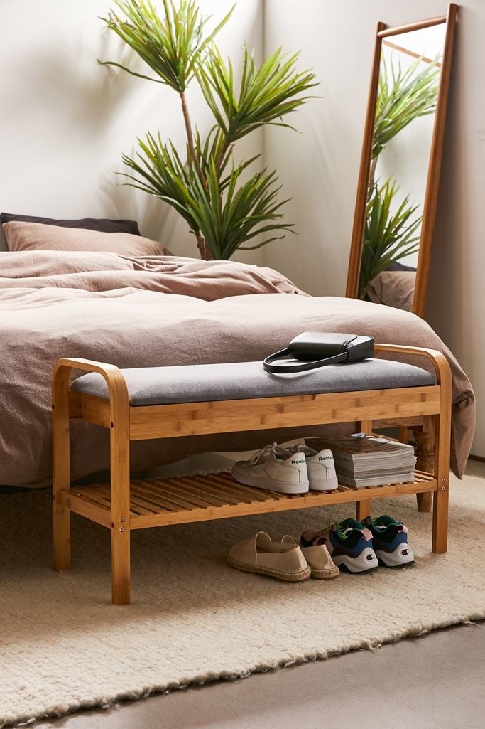 The rectangular bench with a fabric cushion on top and a shelf with shoes stored on it near the bottom