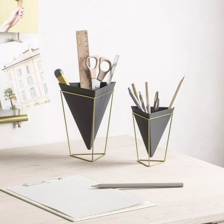 Black cone-shaped planters with gold metallic frame sitting on a desk holding pens, scissors, and office supplies