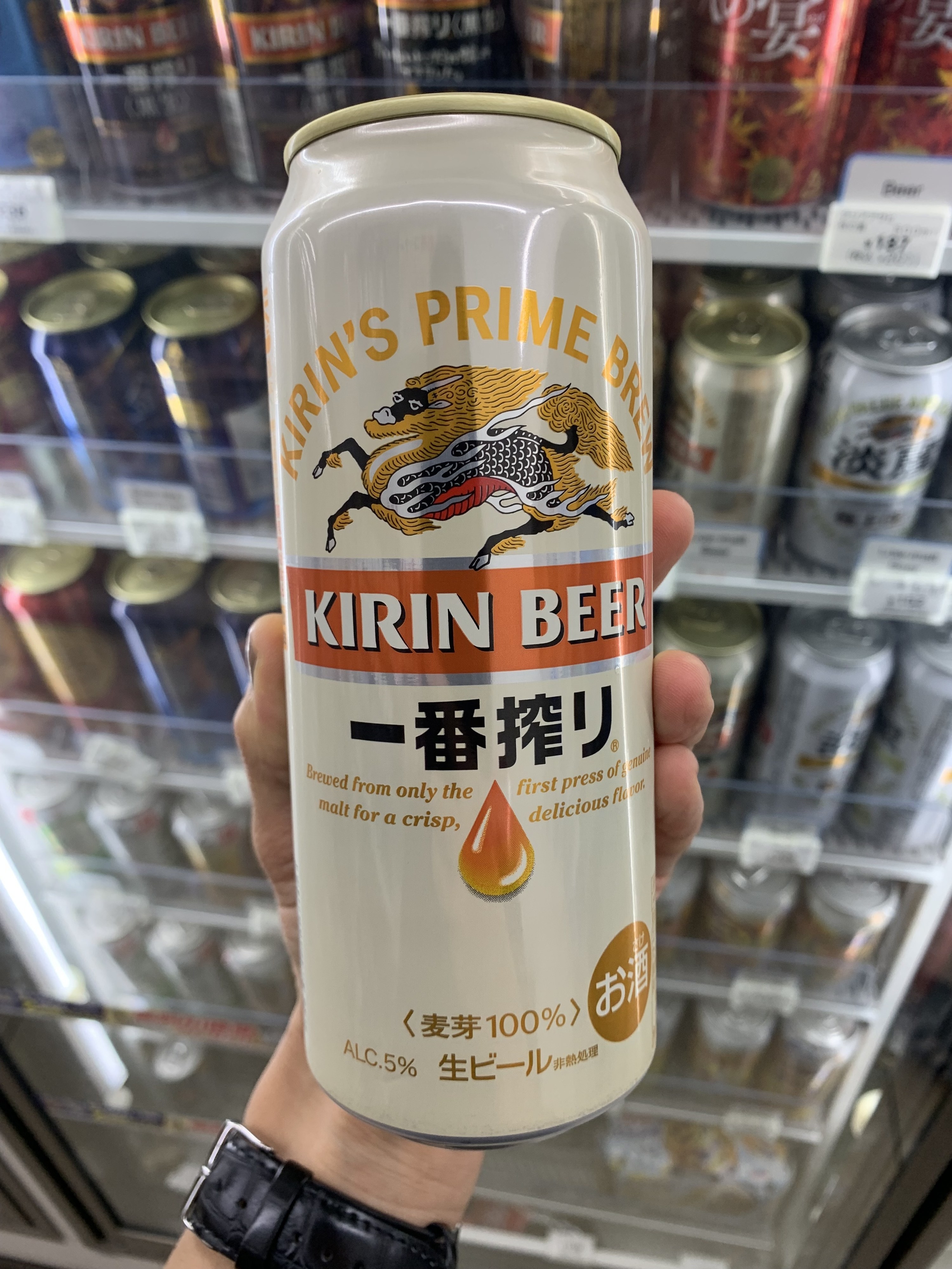 A can of Kirin held up in front of a fridge full of different beer varieties