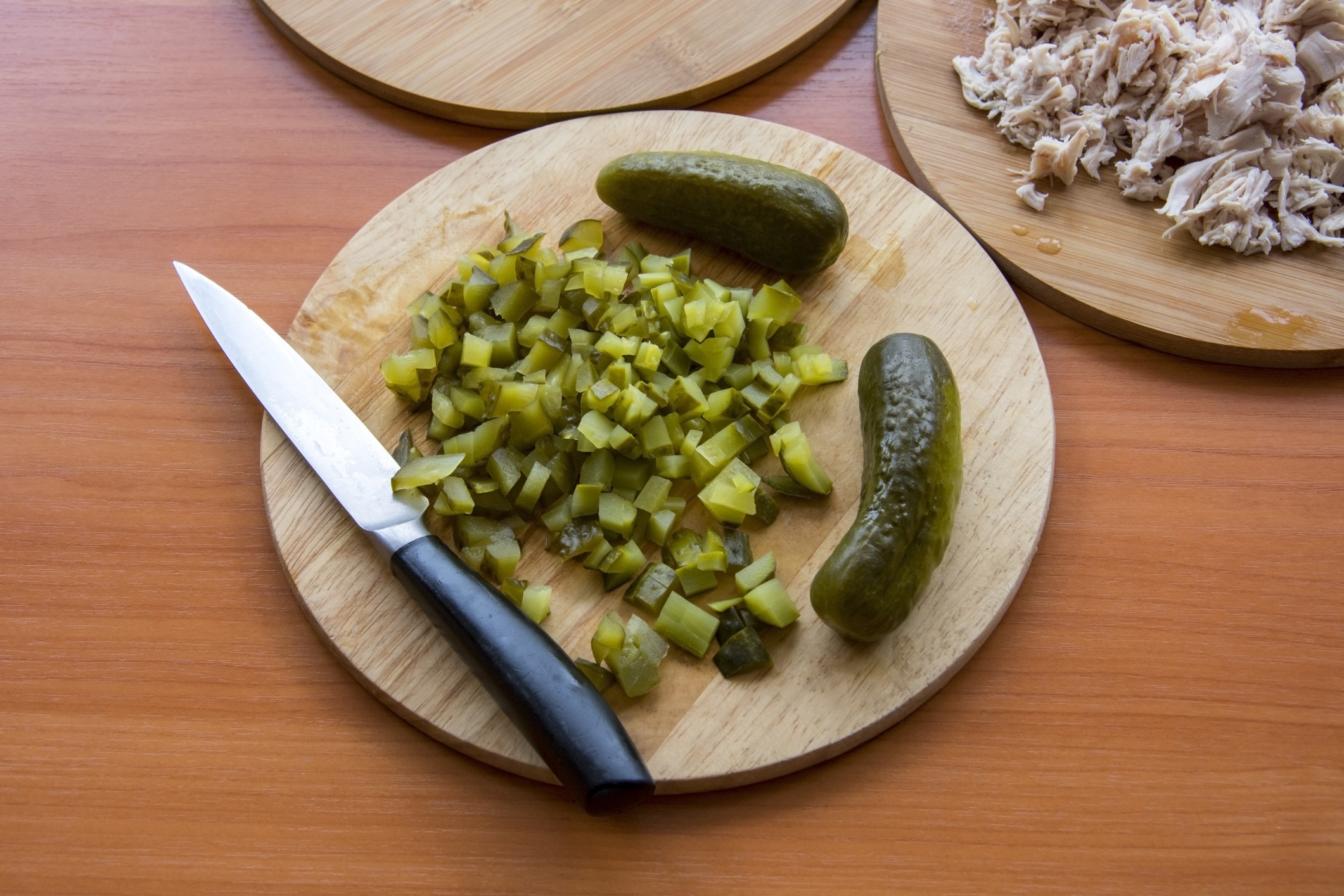 A wooden cutting board topped with thinly chopped pickles.