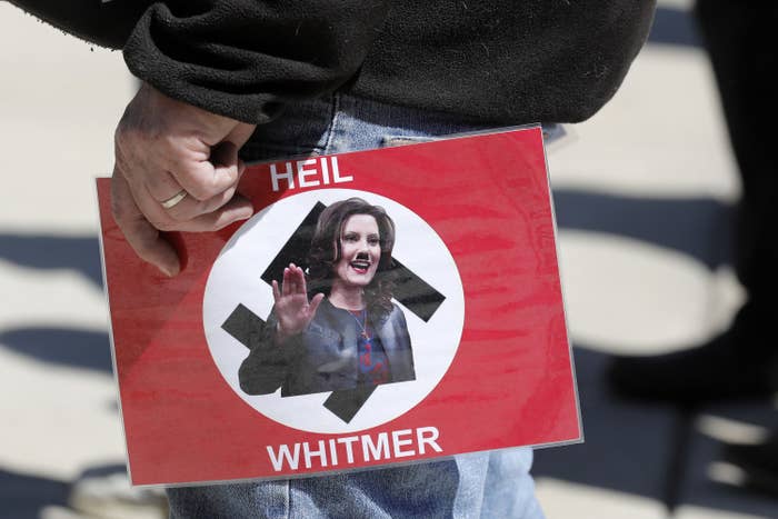 Someone holds a sign with the flag of Nazi Germany; over the swastika in the center, Gretchen Whitmer appears with a photoshoppted Hitler mustache, appearing to make a &quot;Heil Hitler&quot; salute; the sign reads &quot;Heil Whitmer&quot;