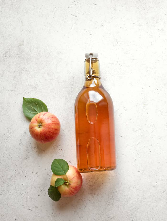 A bottle of apple cider vinegar on a countertop with two apples next to it.