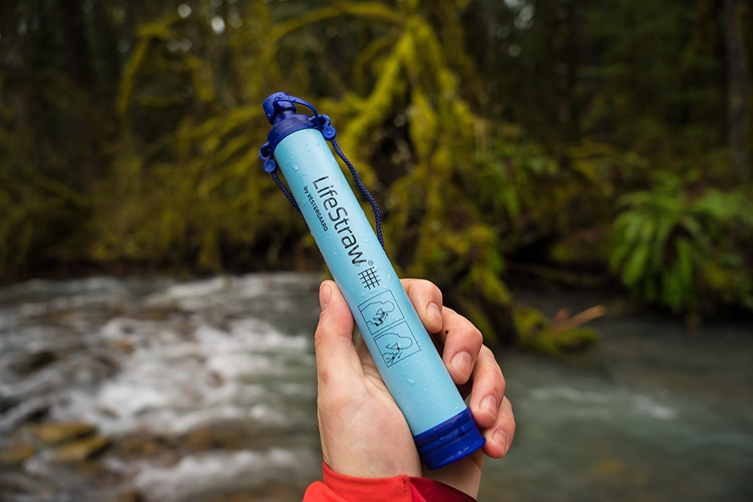 A person holds a life straw in front of an outdoor water setting