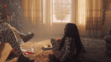 a gif of taylor swift and her fake husband and daughter hugging in matching christmas pajamas in front of a christmas tree in the lover music video