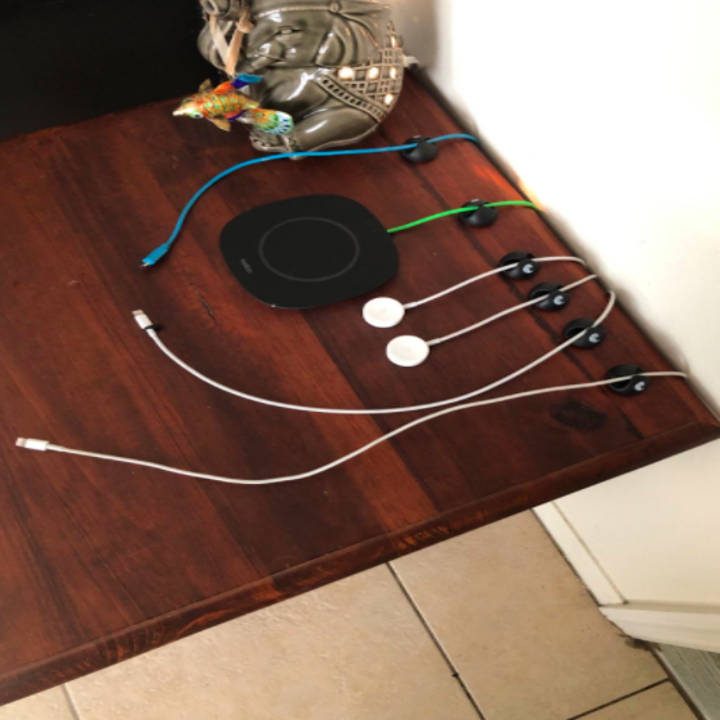 Reviewer uses black cable clips to organize blue, white, and green charging cords on the side of their dark wood desk