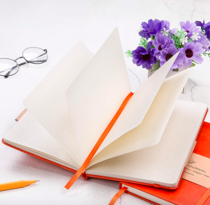 小橙杂志与空白页表旁边一个橙色的钢笔,眼镜,和紫色的花