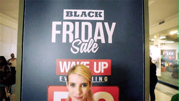 GIF of Emma Roberts from Scream Queens smiling in front of a sign that says &quot;Black Friday Sale&quot;