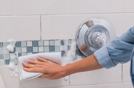 A towel wipes the spray, which is foamy, from a tiled wall
