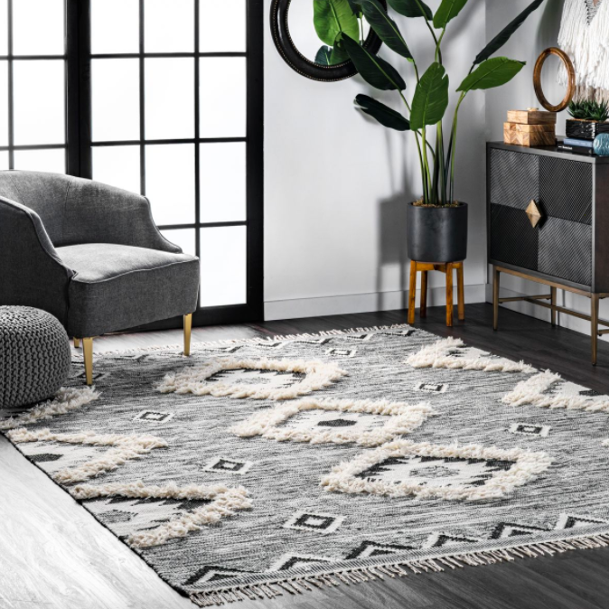 Shaggy Moroccan-style gray, white, and black square rug next to gray armchair, black planter, and black and gray chest