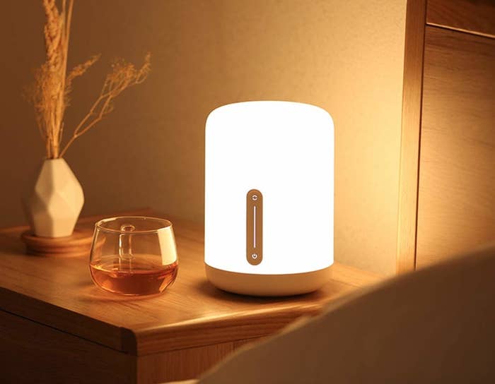 A Mi Smart Lamp placed on a bedside table next to a cup and a vase