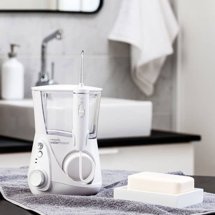 A close up of the water flosser next to a bar of soap in a bathroom