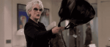 Gif of Meryl Streep from The Devil Wears Prada taking off coat and purse and dropping them on her assistant&#x27;s desk 