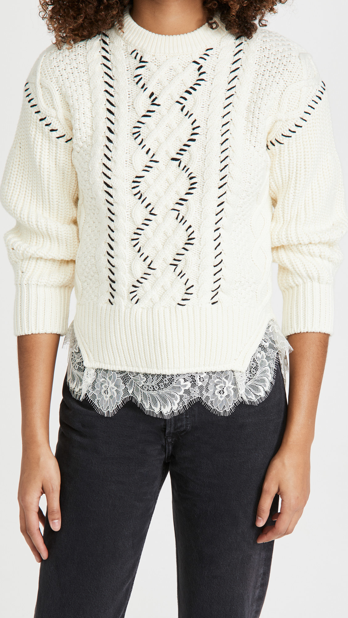 A model wearing the white cable knit sweater with black stitch details and white lace at the bottom with black jeans