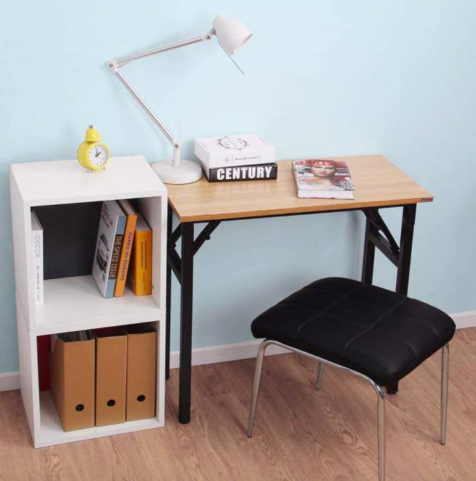 Folding desk with wooden top and black legs next to a black stool and small white bookcase